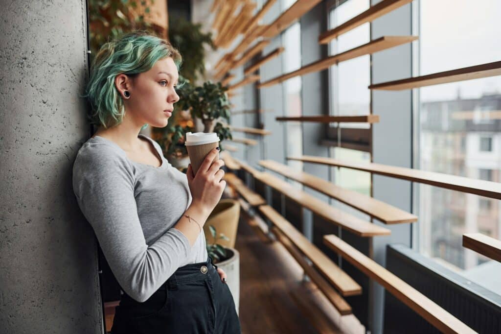 Alternative girl in casual clothes and with green hair standing indoors at daytime