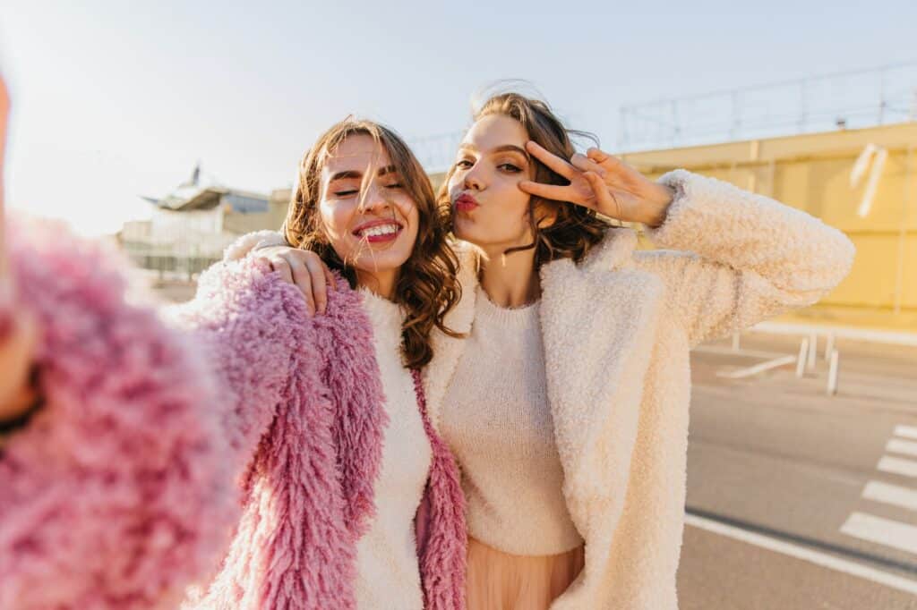 Emotional girls posing in autumn day. Outdoor shot of best friends making selfie on the street